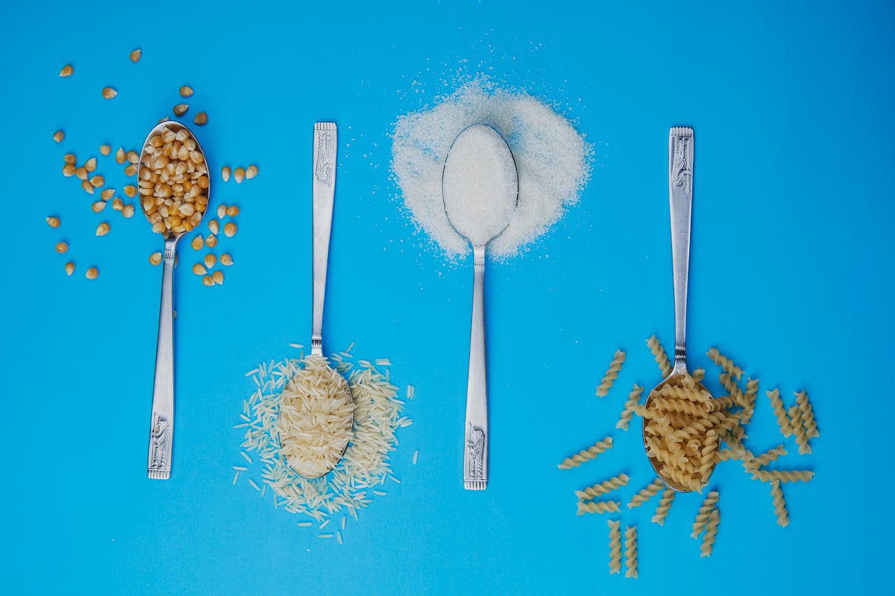 services-02 Four spoons with popcorn, rice, sugar, and pasta on a blue background. Perfect for food-related projects.