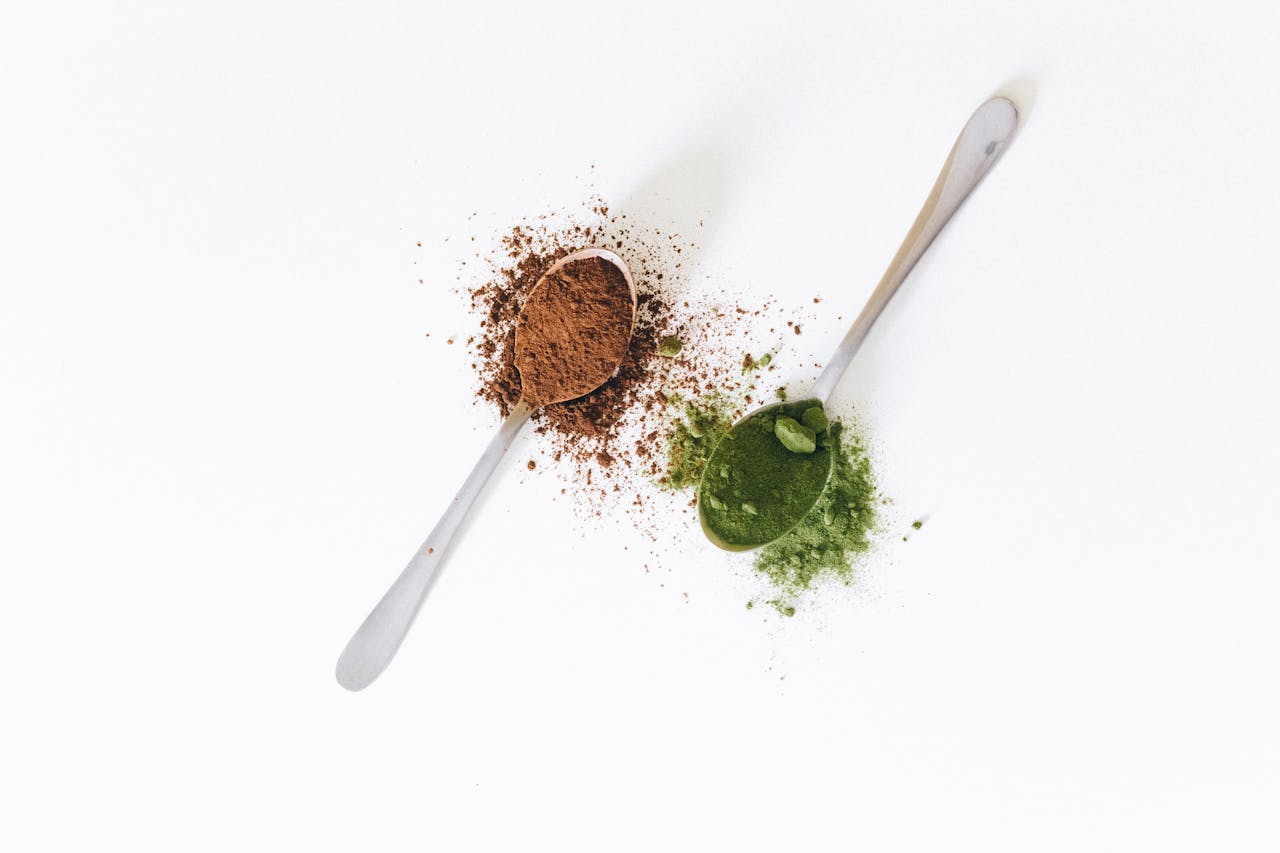 Close-up of spoons with cocoa and matcha powder on a white surface, perfect for food and health themes.